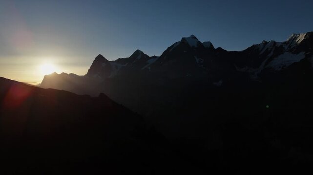 Drone view of jagged alpine peaks near M&uuml;rren and Birg at sunrise, with layered silhouettes and clear sky in the Swiss Alps.