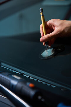 Expert mechanic prepares the glass damage for treatment by using a specialized precision scriber tool to clean the damage point during a windshield repair service