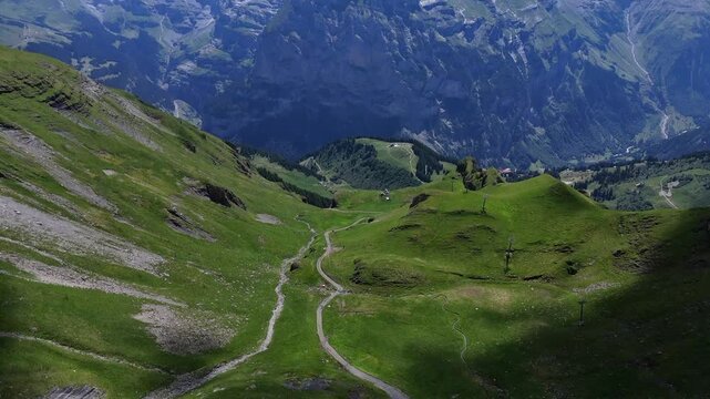 Drone view of winding footpath across green Swiss alpine slopes with dramatic Berner Oberland mountain backdrop near M&uuml;rren and Birg.