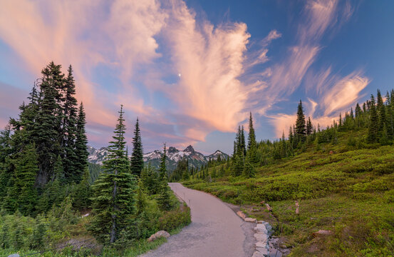 Paved trail through mountain forest with dramatic sunset clouds