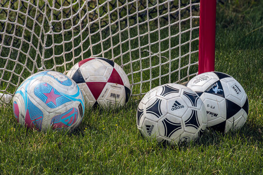 Sporting Goods in a recreational grass field, with different brand soccer balls, rsting near a goal nest.