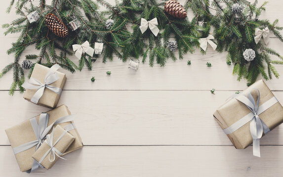 Christmas decoration, gift boxes and garland frame concept background, top view with copy space on white wood table surface. Christmas ornaments and presents border