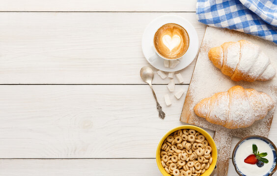 Traditional french breakfast menu background. Yogurt with fresh berries, cup of coffee, muesli and croissants on wooden table, top view, copy space