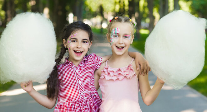 Happy girlfriends enjoying cotton candy in amusement park, embracing and smiling at camera, copy space