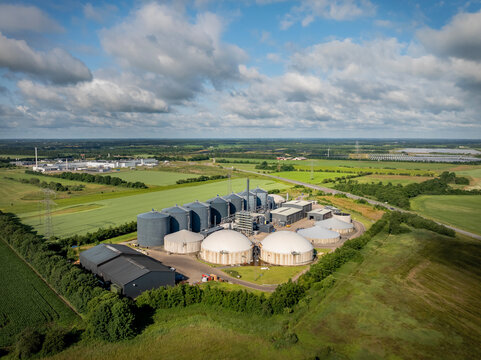 Aerial view of  biogas plant with anaerobic digesters, storage tanks, and renewable energy infrastructure integrated into a rural landscape.