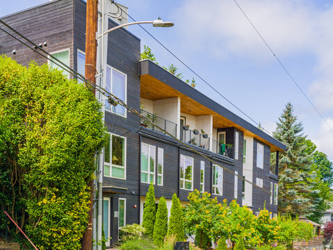 Modern dark grey apartment building with wooden balcony and greenery