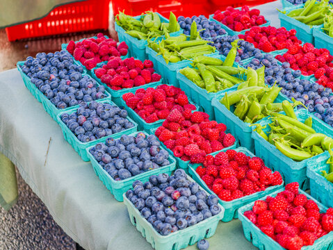 Fresh blueberries, raspberries, and snap peas in blue crates at a farmers market
