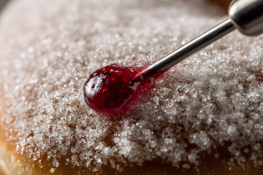 Macro photograph of a metal nozzle injecting vibrant raspberry jelly into a sugar-dusted donut