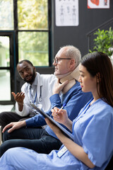 Obraz premium Senior patient wearing a neck brace is examined by healthcare workers while a nurse writes notes and a doctor provides clinical care support.