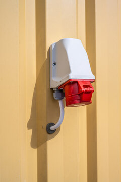 Red industrial power socket mounted on yellow wall.