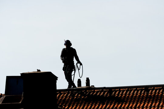 Silhouette of worker standing on tiled roof with safety gear.