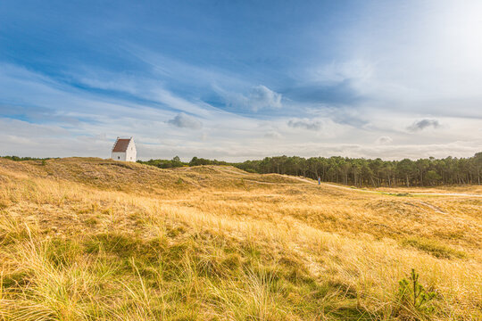 White chapel in windswept dune landscape under dramatic sky.