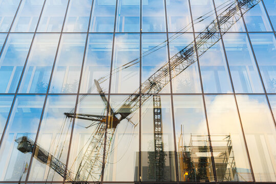 Construction crane reflected in modern glass office facade.