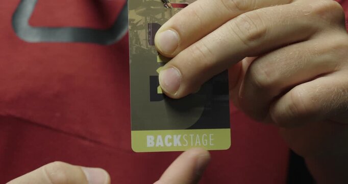 Person pointing at a backstage pass badge, showing event access and exclusive entry identification.