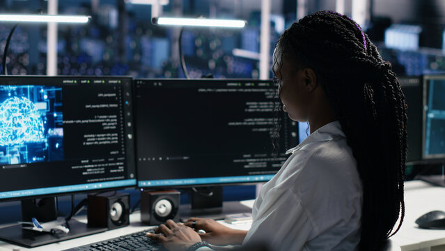 Server facility IT administrator working on AI network software development. African American woman in data center rolling out ML technology working with workstation.