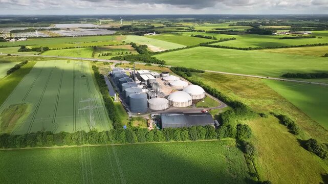 Aerial footage of biogas plant with anaerobic digesters, storage tanks, and renewable energy infrastructure integrated into a rural landscape.