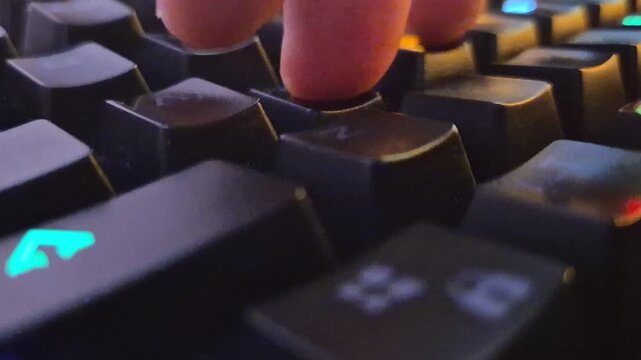 A low angle, closeup, macro shot of a finger typing on a black, RGB-backlit, mechanical gaming keyboard in a dark room.