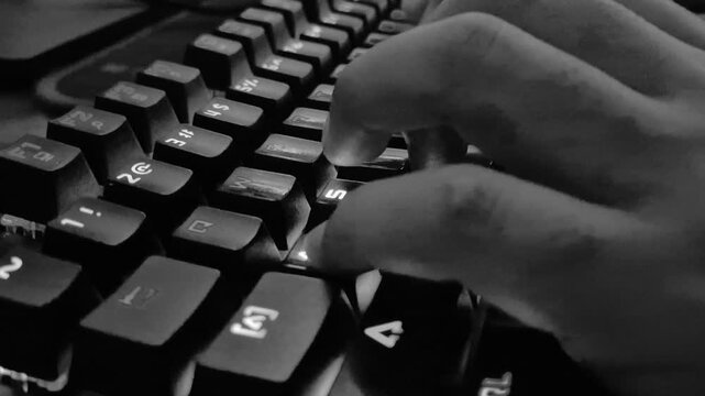 A close-up view of a hand typing and gaming on a mechanical keyboard is shown in monochrome black and white.
