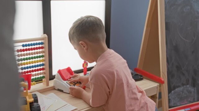 Boy pressing buttons on a toy cash register with visible hands at a play table in building; curiosity learning.