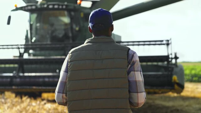 Rear view of a farmer walking toward a combine harvester during harvest season, representing agriculture, determination, modern farming, rural work and the start of another day in the field.