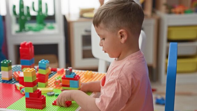 Boy stacking colorful plastic blocks with right hand on play table in building; concentration creativity.