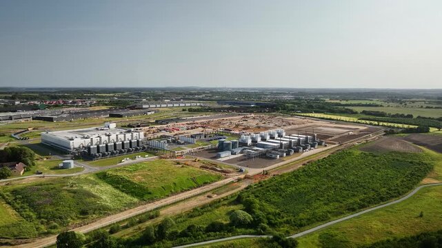 Aerial footage of modern data center complex with adjacent energy infrastructure, utility facilities, and expansion areas under construction within a large industrial park.
