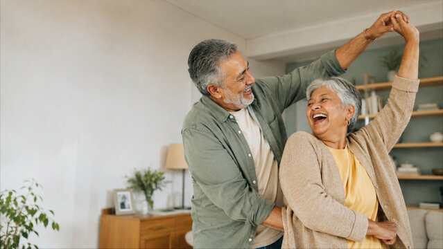 Happy senior Hispanic couple laughing while dancing together in their living room