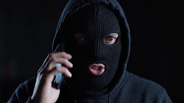 Criminal wearing a ski mask talking on a mobile phone in the dark