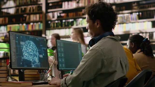 Asian student working with AI brain display on desktop monitor in library computer lab, surrounded by books stacked across wooden study table.