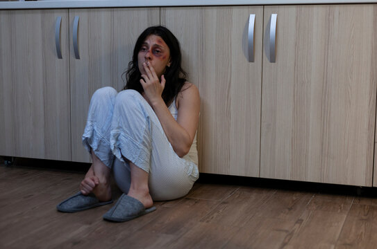Crying wife sits on the floor with facial bruises after domestic violence, capturing fear, trauma and an unhappy marriage with an aggressive husband, linking injured wife and domestic abuse.