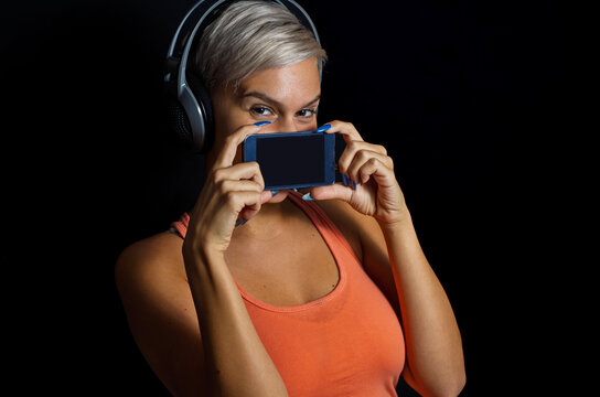 Girl whit short gray hair and headphones holding smartphone over her mouth, black background 