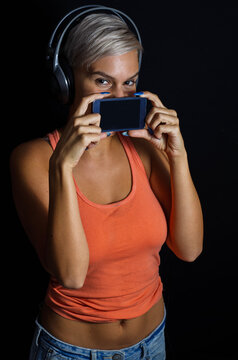 Girl whit short gray hair and headphones holding smartphone over her mouth, black background 