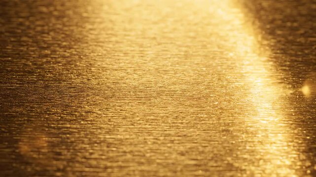 Cinematic close up of brushed metallic gold surface with warm light rays scanning across the textured metal background