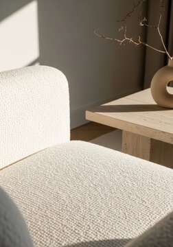 White armchair with textured fabric near beige travertin coffee table. Modern living room interior with sunlight and shadow. Minimalism, comfort and home decoration concept.