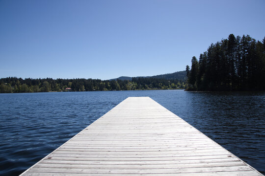 Wooden Pier Stretching into Calm Lake under Clear Blue Sky