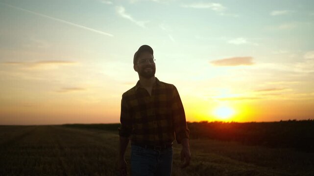 A man walks through a field as the sun sets in the background. He appears to reflect on his day while enjoying the beauty of the landscape. The warm colors fill the sky as night approaches.