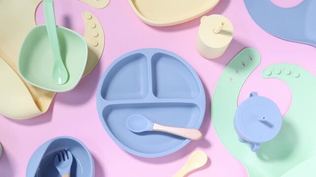 Set of baby tableware on pink background, flat lay. Camera moving right