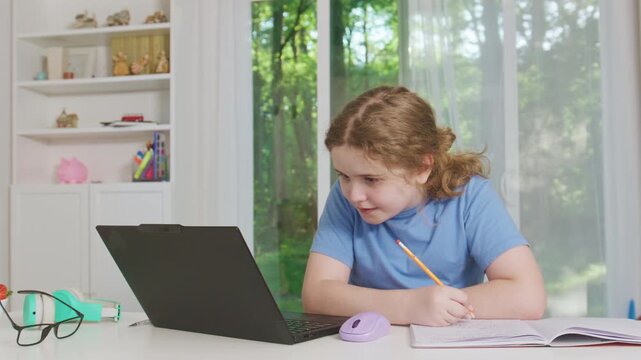 Kid learning in home school. Online learning and homework writing. Focused student in home education. Student writing in notebook. Remote education with laptop screen. Modern school workspace.