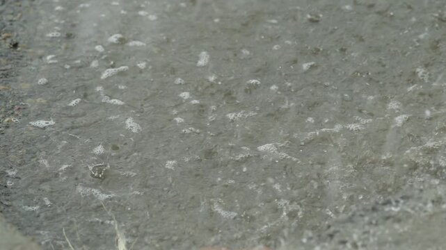 Heavy rain drops falling on a large puddle on concrete ground