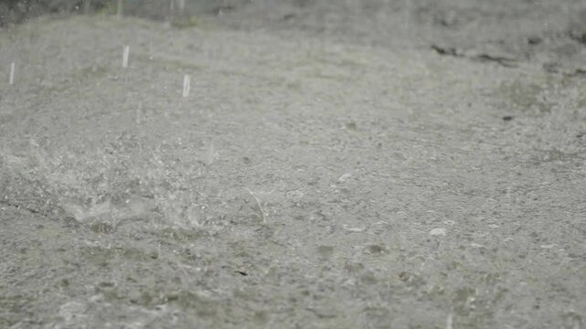 Heavy rain drops falling on a large puddle on concrete ground