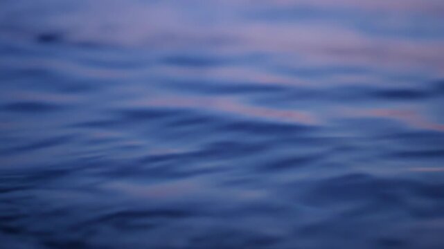 Slow motion close up of tranquil water surface with blue hour reflections and gentle rippling patterns at twilight
