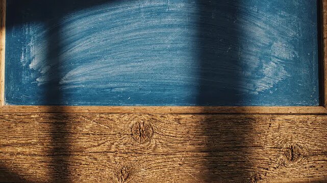 Top down view of empty rustic wooden tabletop with soft light shadows moving across a textured blue chalkboard background
