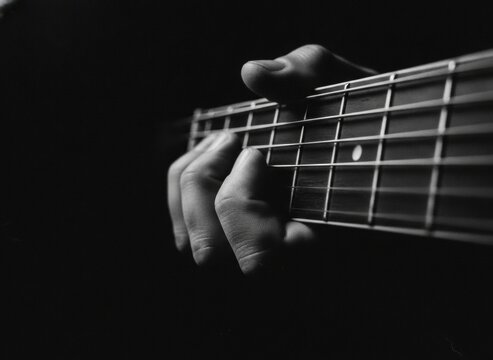 Close-up of a hand playing an acoustic guitar in black and white with dramatic lighting