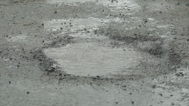 Rain drops falling into a muddy puddle on broken asphalt.