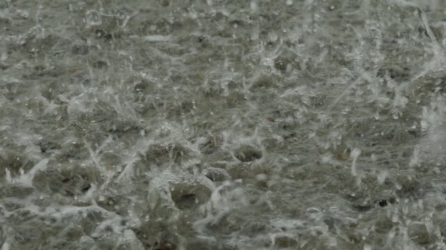 Heavy rain drops falling on a large puddle on concrete ground