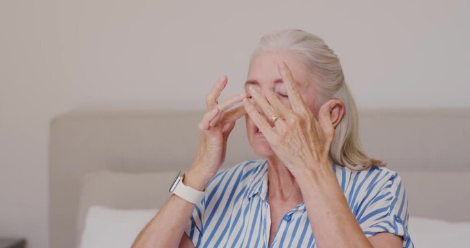 Senior woman on bed rubbing eyes, massaging temples easing pain, wearing shirt and smartwatch