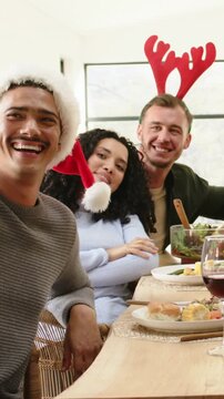 Vertical video: Turning after phone prompt group at table leaning, laughing with Santa hat, antlers