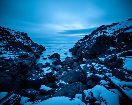 Paysage cotier hivernal spectaculaire avec rochers enneiges et glaces au bord d'une mer bleue turquoise sous un ciel dramatique, nature sauvage et minerale en bord de mer arctique