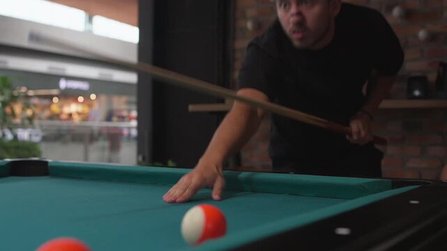 Focused young man hitting a cue ball playing billiards
