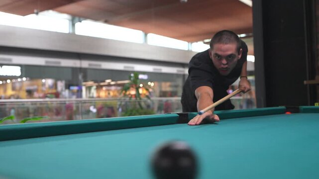 Focused young man playing billiards sinking a shot